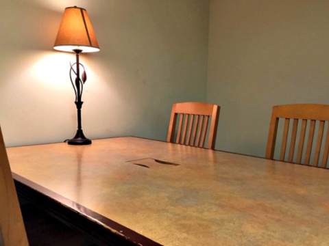 photo of a table with a lit lamp, two wooden chairs are visible